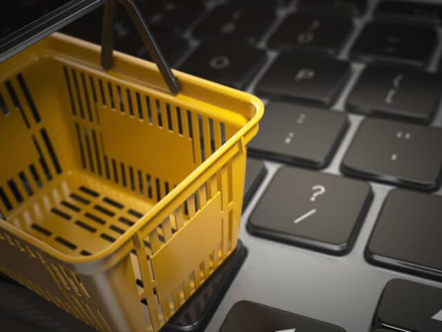 E-commerce, online shopping, internet purchases concept. Yellow shopping basket on computer laptop keyboard,